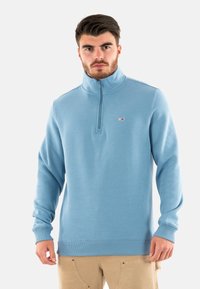 Felpa con zip azzurro chiaro e colletto alto, con polsini a costine. Presenta un piccolo logo sul petto. Realizzata in un tessuto morbido e strutturato.