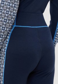 Närbild av mörkblå tajta leggings med ljusblå sömmar och mönstrade blå och vita tygpaneler på sidorna och ärmarna.