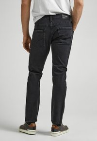 Černé džíny s úzkým střihem, s zadními kapsami s decentním designem a koženým štítkem na pase. Nosené s šedými teniskami.