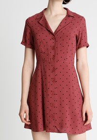 Vestido burdeos de manga corta con collar; presenta lunares negros y una parte delantera abotonada; hecho de una tela suave.