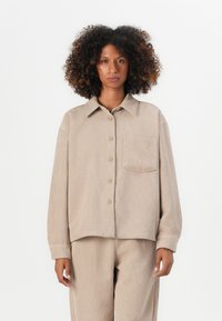 Camicia in corduroy beige con chiusura a bottoni, vestibilità rilassata, colletto a punta, taschino sul petto e texture a coste.