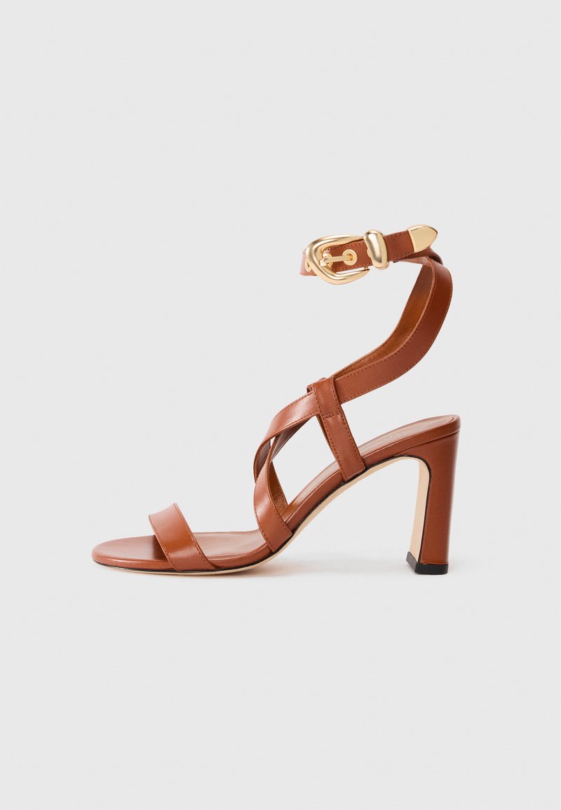 Sandal cu toc din piele maro, cu un design cu curele și cataramă la glezna. Prezentă un spate închis și un toc înalt, robust. Textură netedă.