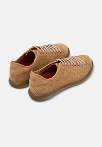 Zapatillas de cuero perforado beige con cordones claros y suela de goma marrón. Presentan una puntera redondeada y una marca mínima en el talón.