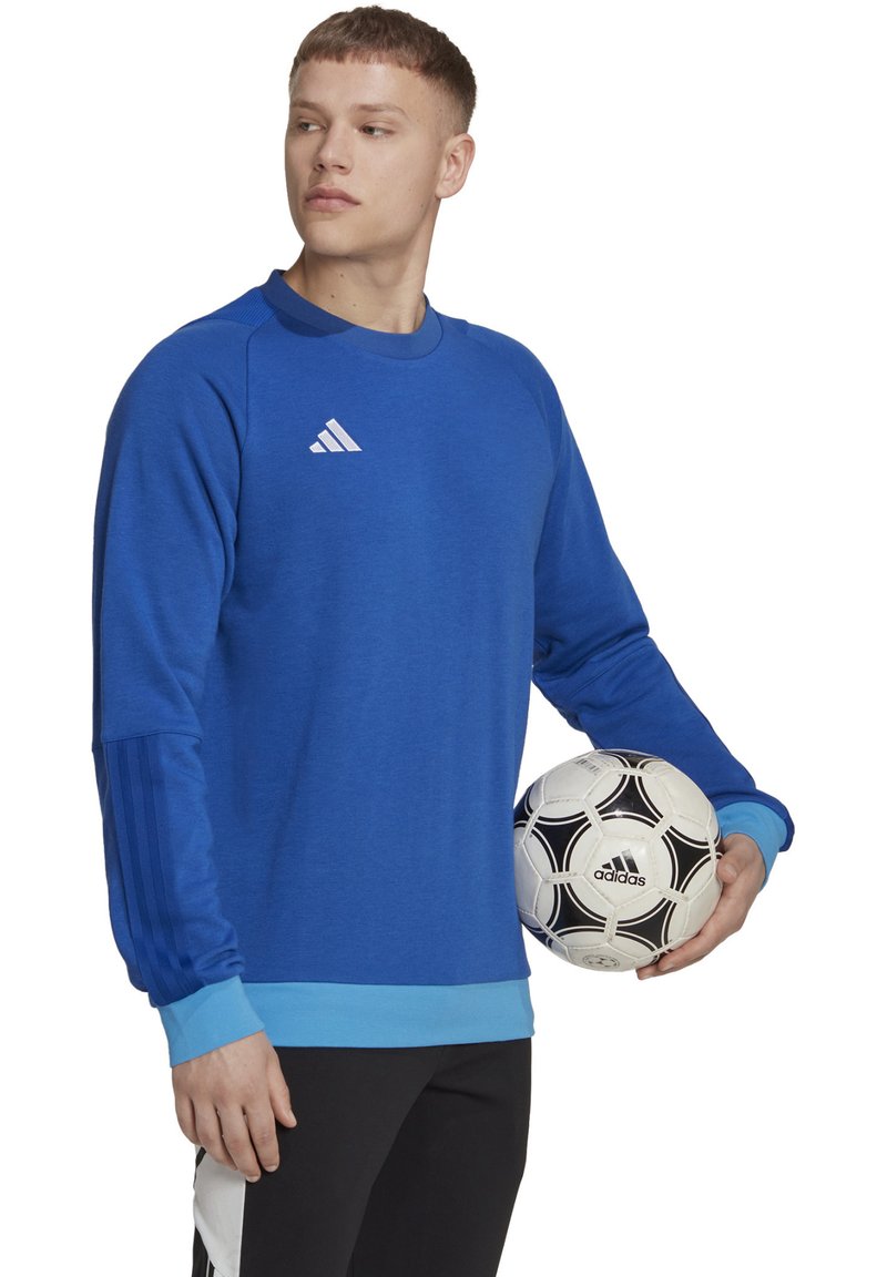 Blauwe sweatshirt met lange mouwen, Adidas-logo op de borst, ribbelmanchetten en -zoom, gladde textuur. Houdt een zwart-wit voetbals bal vast.