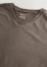 Tricou din bumbac maro, cu decolteu în V și o croială obișnuită. Are o textură moale și un eticheta în interior, care indică brandul și originea.