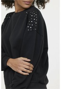 Sweatshirt noir avec des accents texturés et des détails cloutés sur les épaules. Offre une coupe décontractée et un tissu doux.