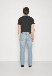 Siniset farkut suoralla lahkeella, haalistuine pesu ja ruskea nahkainen takapatch. Musta t-paita ja mustat lenkkarit täydentävät asun.