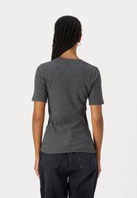 T-shirt grigio a maniche corte con una silhouette aderente e un collo rotondo. Texture liscia; design semplice. Abbinato a jeans scuri.