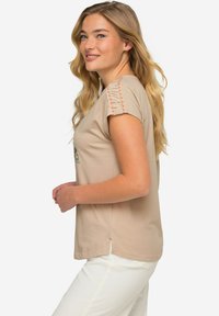 Camiseta corta de color beige claro con mangas cortas, costuras decorativas naranjas en las costuras de los hombros, corte relajado y aberturas laterales en el dobladillo.