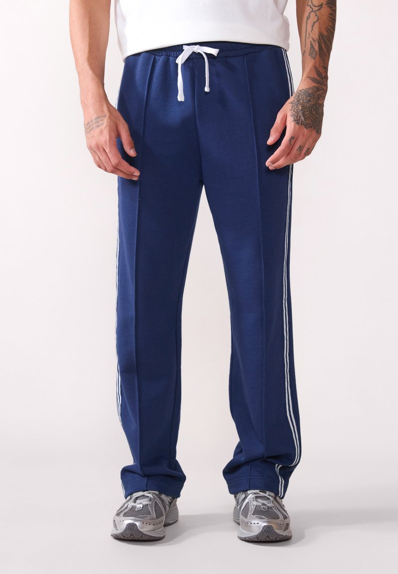 Navy blå joggebukser med hvit snor, med hvite side striper, laget av mykt stoff, med en avslappet passform og elastisk midjebånd.