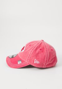 Ružová bavlnená baseballová čiapka s zakriveným okrajom, predným logom na patróne a bielymi štepmi. Obsahuje nastaviteľný popruh a logo na boku.