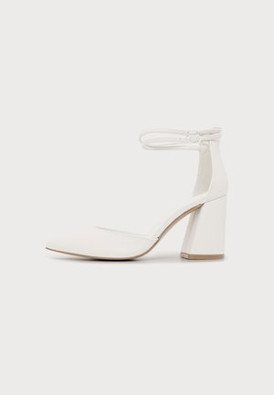 Chaussure blanche pour femme à bout fermé, talon haut bloc et double lanières de cheville avec fermeture à boucle sur fond uni.