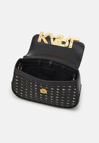 Bolsa cruzada tejida negra con cierre de botón dorado y gran logo KARL dorado en la tapa elevada que muestra un interior vacío.
