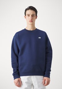 Mörkblå sweatshirt i mjukt tyg, med rundad halsringning, långa ärmar och en liten vit logga på vänster bröst.
