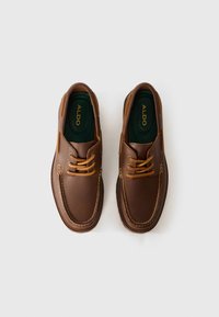 Chaussures en cuir marron avec une texture lisse, bout rond et couture contrastée marron foncé. Elles présentent des lacets beiges et une semelle intérieure verte.