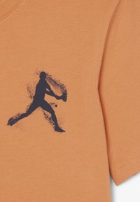Silueta de un jugador de béisbol balanceando un bate hacia una bola, impresa en tinta oscura sobre tela de color naranja claro.