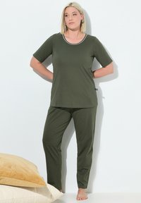 Conjunto de pijama verde oliva con una blusa de manga corta que presenta un escote blanco y pantalones de patrón de lunares. Tejido suave, corte relajado.