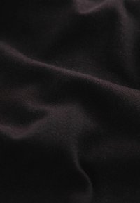 Black fabric showing a soft, slightly textured surface with natural folds and creases, emphasizing its smooth, matte quality.