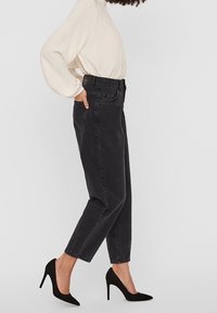 Höga svarta denimjeans med avsmalnande ben, sidofickor och en lätt urtvättning, kombinerat med svarta högklackade skor och en ljus topp.