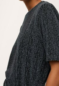 Top nero con texture e finitura lucida, con maniche corte e vestibilità morbida. Il tessuto presenta un delicato motivo a righe.