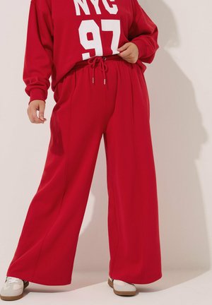 Roter übergroßer Pullover und passende weit geschnittene Hose, beide aus einem glatten Stoff. Der Pullover hat einen weißen Druck "NYC 97", die Hose hat einen elastischen Bund.