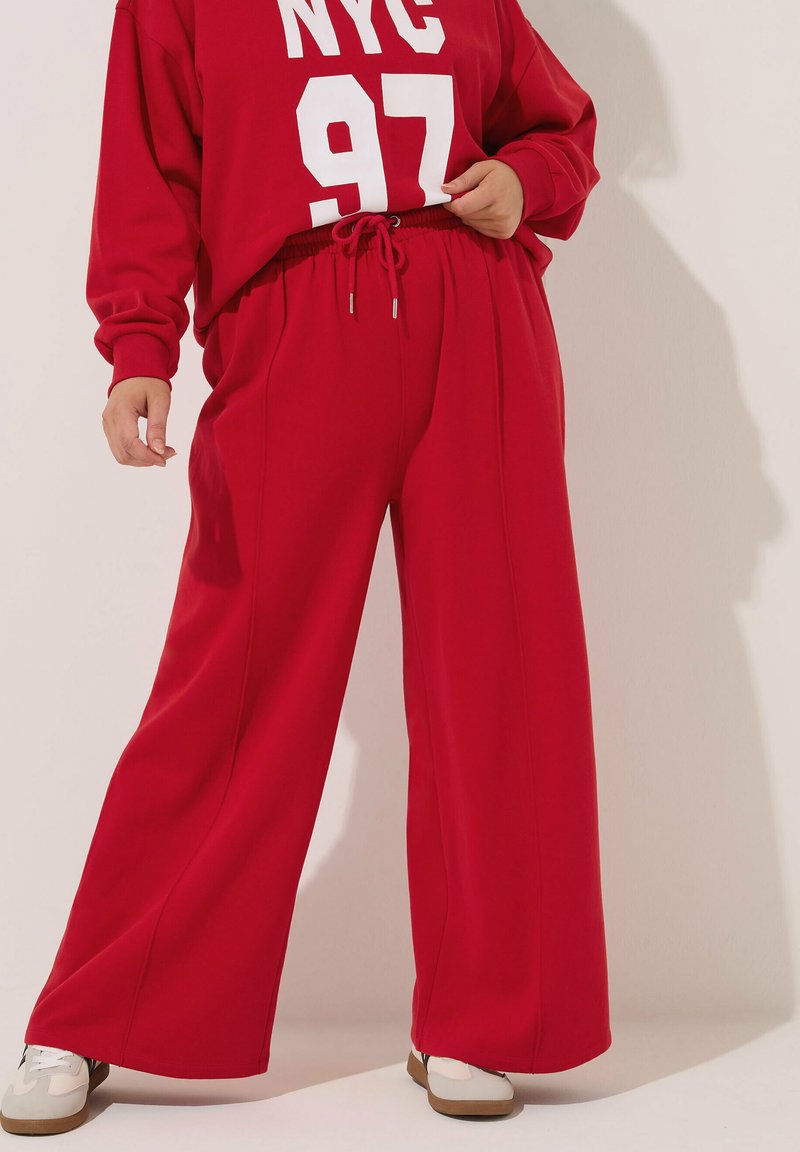 Rode oversized sweatshirt en bijpassende wijde broek, beide van een gladde stof. De sweatshirt heeft een witte "NYC 97" print, de broek heeft een elastische tailleband.