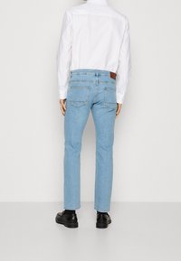 Jeans en denim bleu clair à coupe droite, dotés d'un patch logo en cuir marron sur la ceinture arrière et de deux poches arrière.