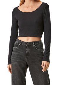 Svart långärmad kort topp med rundad halsringning, tillverkad av mjukt tyg. Stylad med högmidjade mörkgrå jeans och enkla accenter.