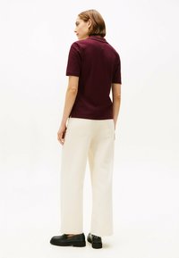 Bordeaux polo shirt med korte ærmer, parret med cremede brede bukser. Sorte loafers bæres, som har en lille guldfarvet accent.