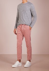 Grauer Strickpullover, rosa Cordhosen und weiße Sneakers. Klassische Passform mit gerippten Bündchen und Saum. Dezente Texturen und Farbtöne.