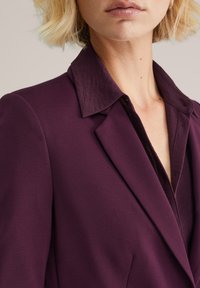 Pflaumenfarbener Blazer mit strukturiertem Design, scharfen Revers und einem leicht strukturierten Kragen, ausgestattet mit einem tiefen V-Ausschnitt und taillierter Passform.