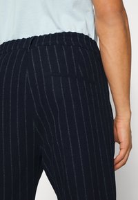 Person med marinblårandiga byxor med elastisk midja och en vit överdel, visad från midjan ner till mitten av låren.