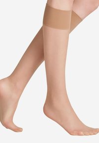 Kniehoge doorschijnende pantykniekousen in een lichtbruine kleur met een gladde textuur en een versterkte band aan de bovenkant, waarbij de tenen en enkel worden blootgesteld.