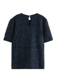 Marineblå blondebluse med korte ærmer, prydet med et blomsterdesign, rund halsudskæring og en nøglehulslukning bagpå med en lille knap.