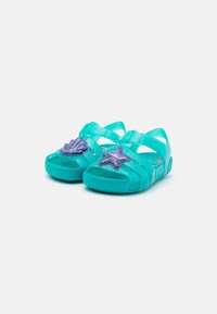 Turkise barne sandaler med glitrende finish, med lilla sjøstjerner og skjell-dekorasjoner på de fremre reimene.