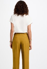 Witte top met korte mouwen en mosterdgele hoge taillebroek, met een soepele textuur en een perfecte pasvorm, voorzien van achterzakken en knoopaccenten.