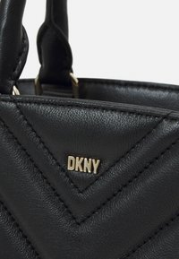 Musta nahkainen käsilaukku, jossa on siksak-kuvio, kullanvärinen "DKNY"-logo ja näkyvät saumat reunoilla.