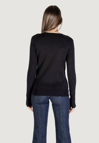 Schwarzer Pullover mit langen Ärmeln und rundem Halsausschnitt, figurbetontem Design, glatter Textur und geripptem Saum. Kombiniert mit blauen Schlagjeans.