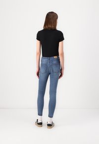 Top scurt negru cu mânecă scurtă, asociat cu blugi skinny albaștri. Blugii au talie înaltă, două buzunare la spate și un mic etichetă pe talie.