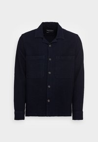 Camicia di lino blu navy con colletto, chiusura a bottoni frontale e due tasche sul petto. Presenta un tessuto testurizzato e maniche lunghe con polsini abbottonati.