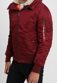 Bordeauxrode gewatteerde bomberjack met een kraag gevoerd met nepbont, een rits aan de voorkant, geribbelde manchetten en een zijzak met decoratieve hardware.