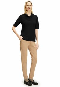 Zwarte poloshirt met korte mouwen, een kraag en drie knopen, gecombineerd met beige tapse broeken en zwarte instappers. Eenvoudig en strak ontwerp.