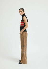 Fekete ujjatlan garbó vízszintes piros és narancs csíkokkal, magas derekú barna farmernadrággal párosítva, amelynek szegélyei kopottak és hátul egy zseb található.