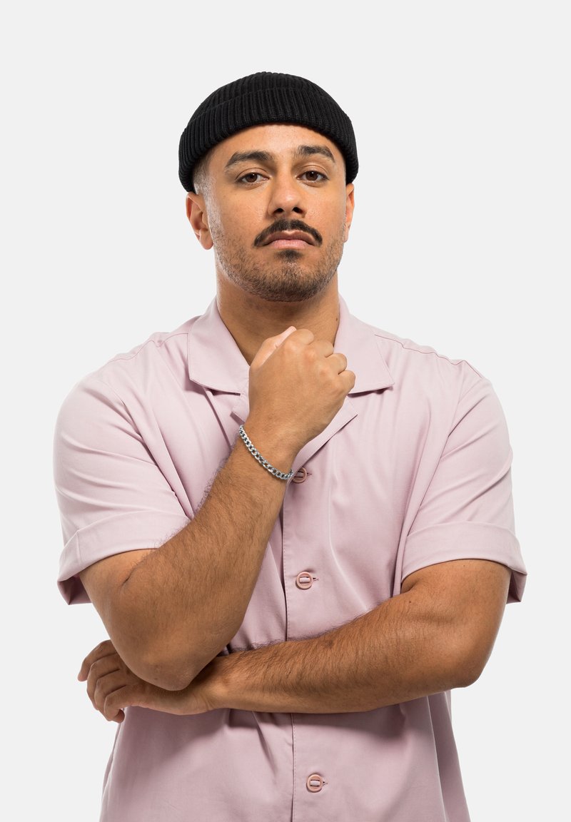 Chemise rose clair à manches courtes avec col, dotée de boutons à l'avant ; portant un bonnet noir côtelé ; un bracelet en chaîne argenté au poignet.
