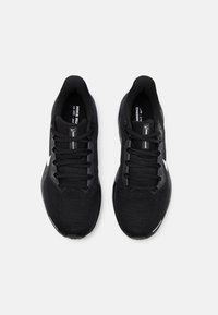 Zapatillas deportivas negras con una parte superior de malla transpirable, punta redondeada, cordones planos y un logo de Nike en blanco en el lateral.