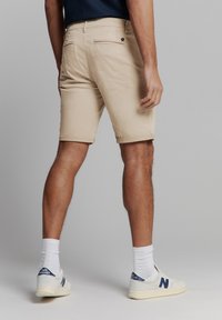 Beige katoenen shorts met omgeslagen pijpen, achterzakken met knopen en een aansluitend ontwerp, gecombineerd met witte sportschoenen en sokken.