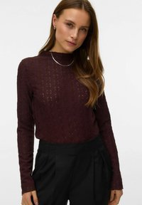 Långärmad, texturerad topp i vinrött med polokrage, med ett diskret geometriskt mönster och en figurnära silhuett. Matchad med svarta byxor.