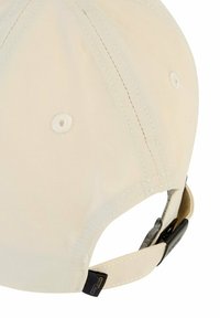 Beżowa czapka z sześcioma panelami, białym haftem i regulowanym paskiem. Posiada małą łatkę z logo po boku oraz otwory wentylacyjne wzdłuż korony.