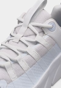 Κοντινή λήψη λευκού αθλητικού παπουτσιού με ύφασμα από δίχτυ, κορδόνια με θηλιές και λεπτομέρειες με ιμάντα στο επάνω μέρος, που αναδεικνύει τα πλευρικά και μπροστινά σχεδιαστικά στοιχεία.