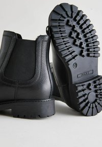 Botas de tobillo de cuero negro con paneles laterales elásticos, superficies texturizadas y suelas de goma resistentes con un patrón de banda de rodadura profundo para mayor tracción.